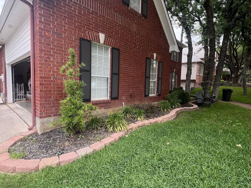 Crisp flower bed edge with fresh dark mulch curving along a red brick home