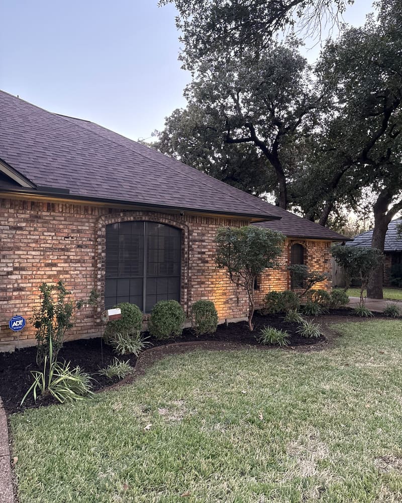 Landscape beds with fresh mulch and lighting at dusk around a brick home