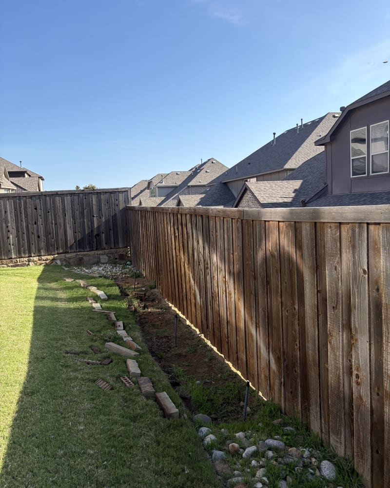 Stone border and new plantings installed along a backyard cedar fence